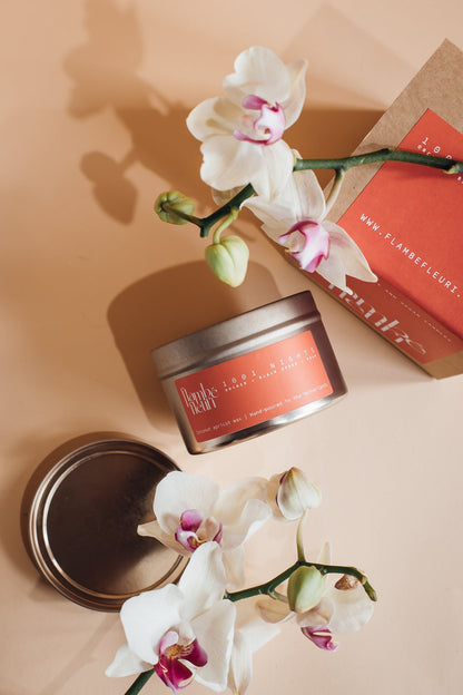 Flambé Fleuri 1001 Nights Candle in decorative tin with intricate floral design, emits warm, inviting glow.